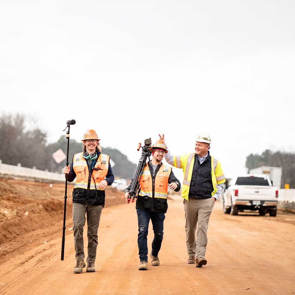 Three team members joke around on a dirt road near a truck.