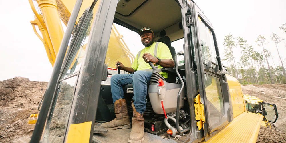 Man in yellow safety shirt operates excavator at construction site.