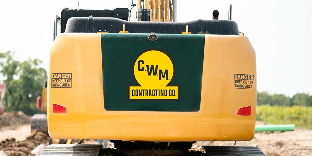 Yellow excavator rear with CWM logo and danger signs.