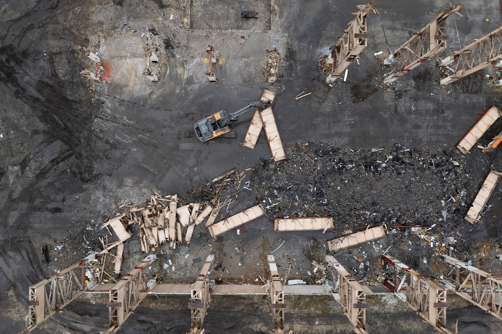 Aerial view: excavator clearing debris among fallen steel beams.