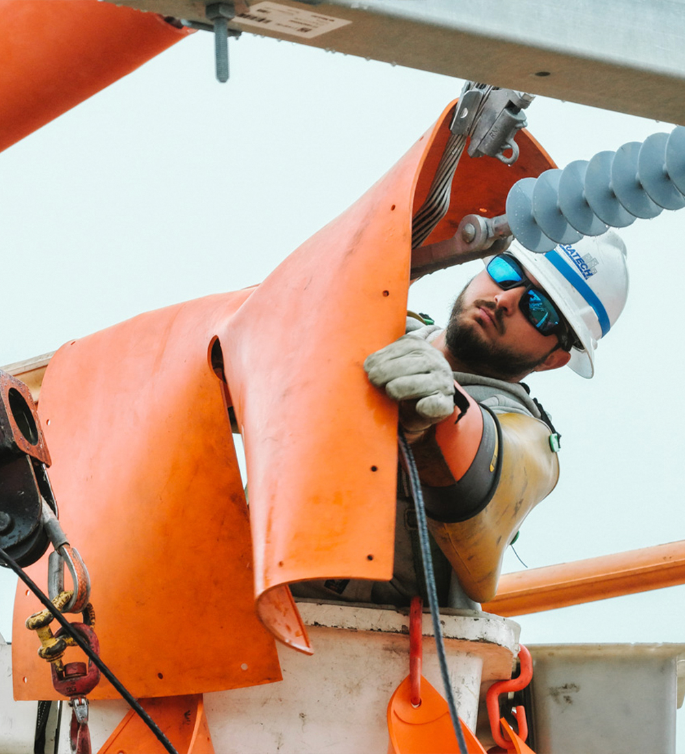 Utility worker in helmet installs orange cover from raised bucket.