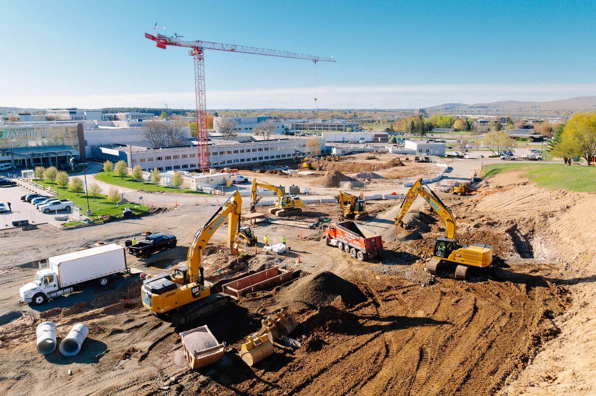 Construction site with trucks, excavators, crane near buildings.