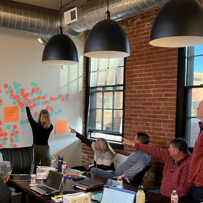 Woman places sticky notes on wall as colleagues point.