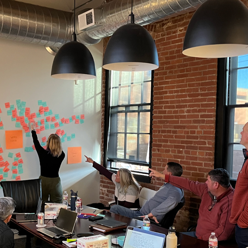 Woman places sticky notes on wall as colleagues point.