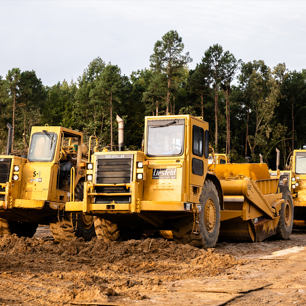 Yellow construction vehicles, including a scraper, parked on mud.