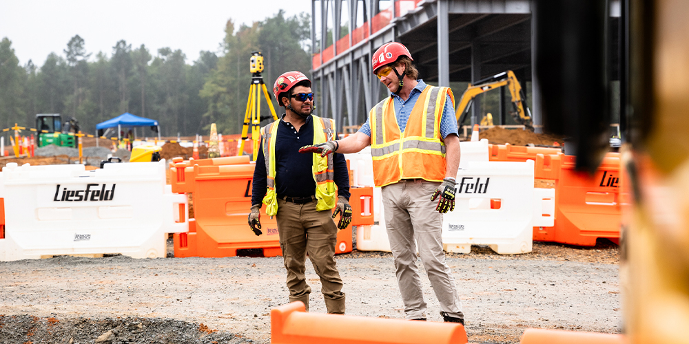 Two workers in safety gear talk at a construction site.