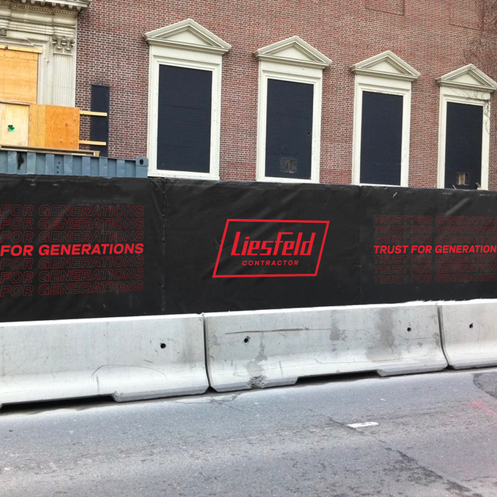 Construction site, black Liesfeld Contractor banner beside boarded brick building.