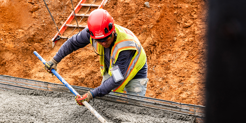 Worker in safety gear spreads wet concrete at worksite.