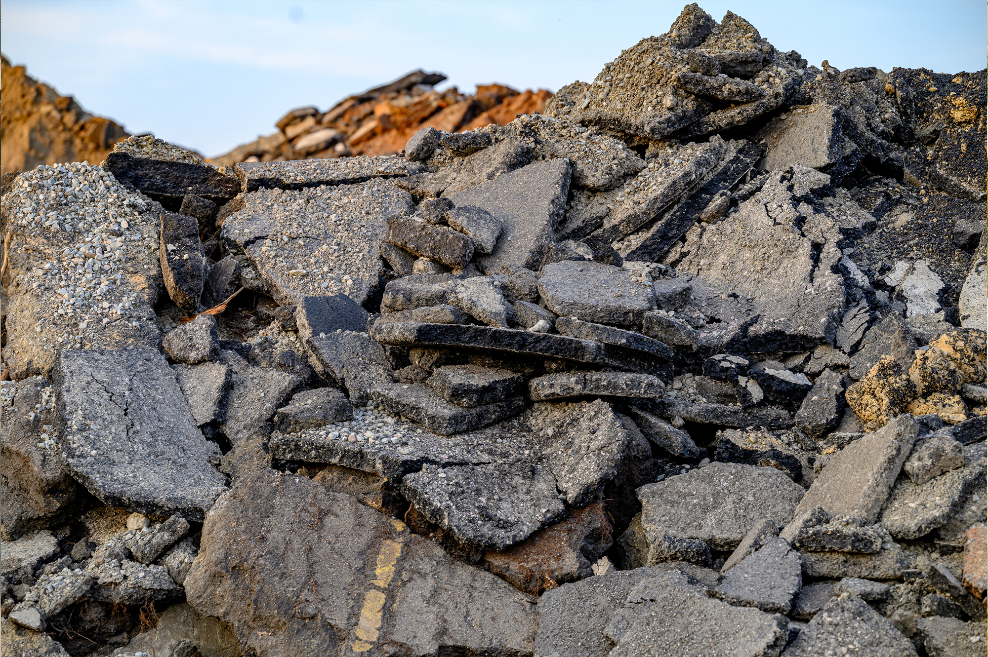 Broken asphalt and gravel beneath a clear blue sky.