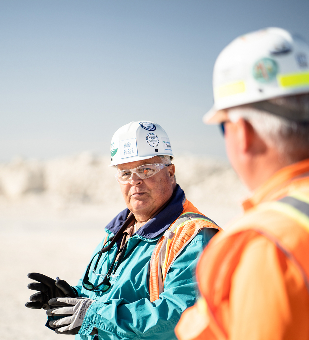 Two construction workers in safety gear talk at a work site.