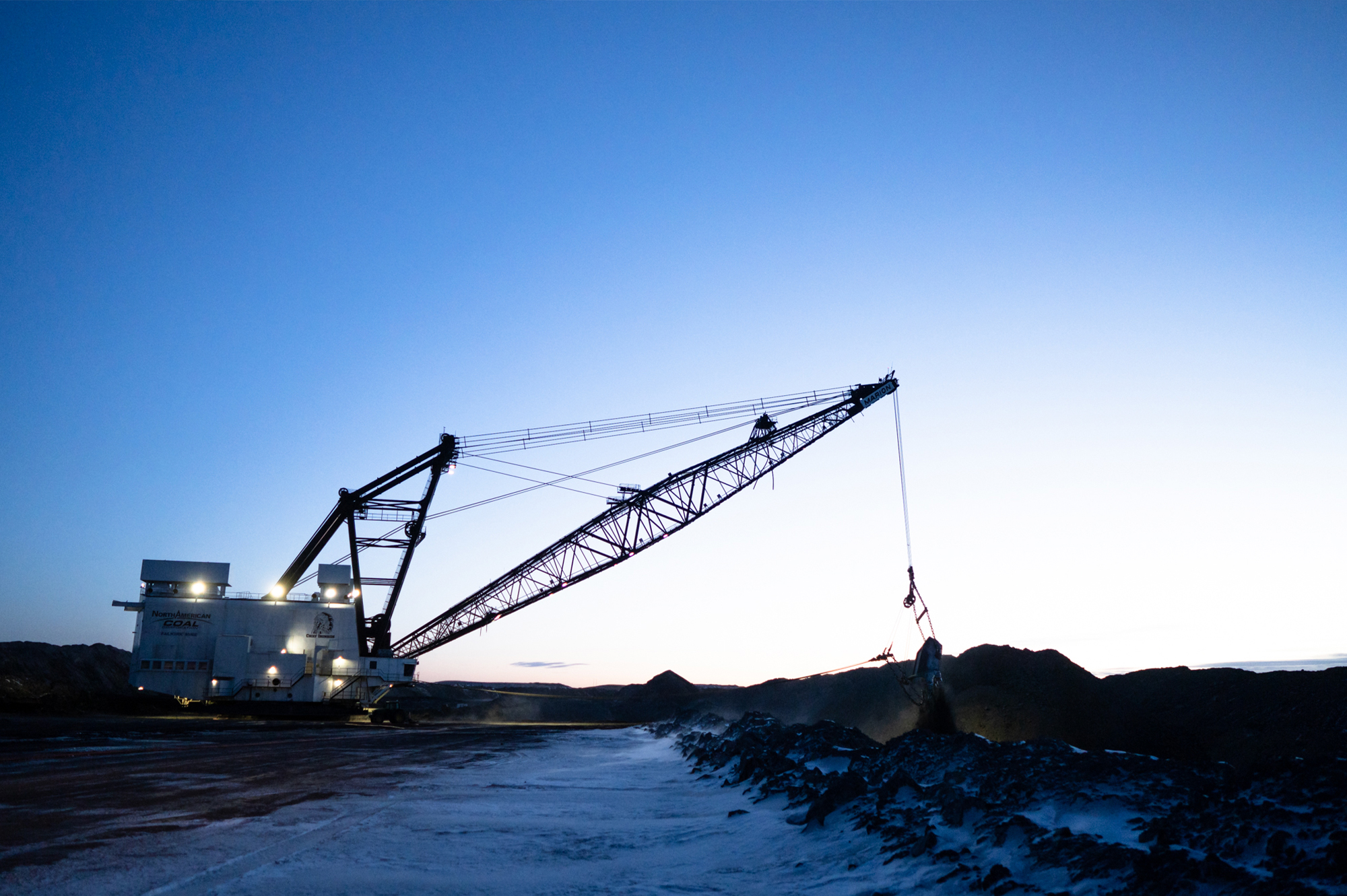 Dragline excavator lifts earth at mining site at dusk.