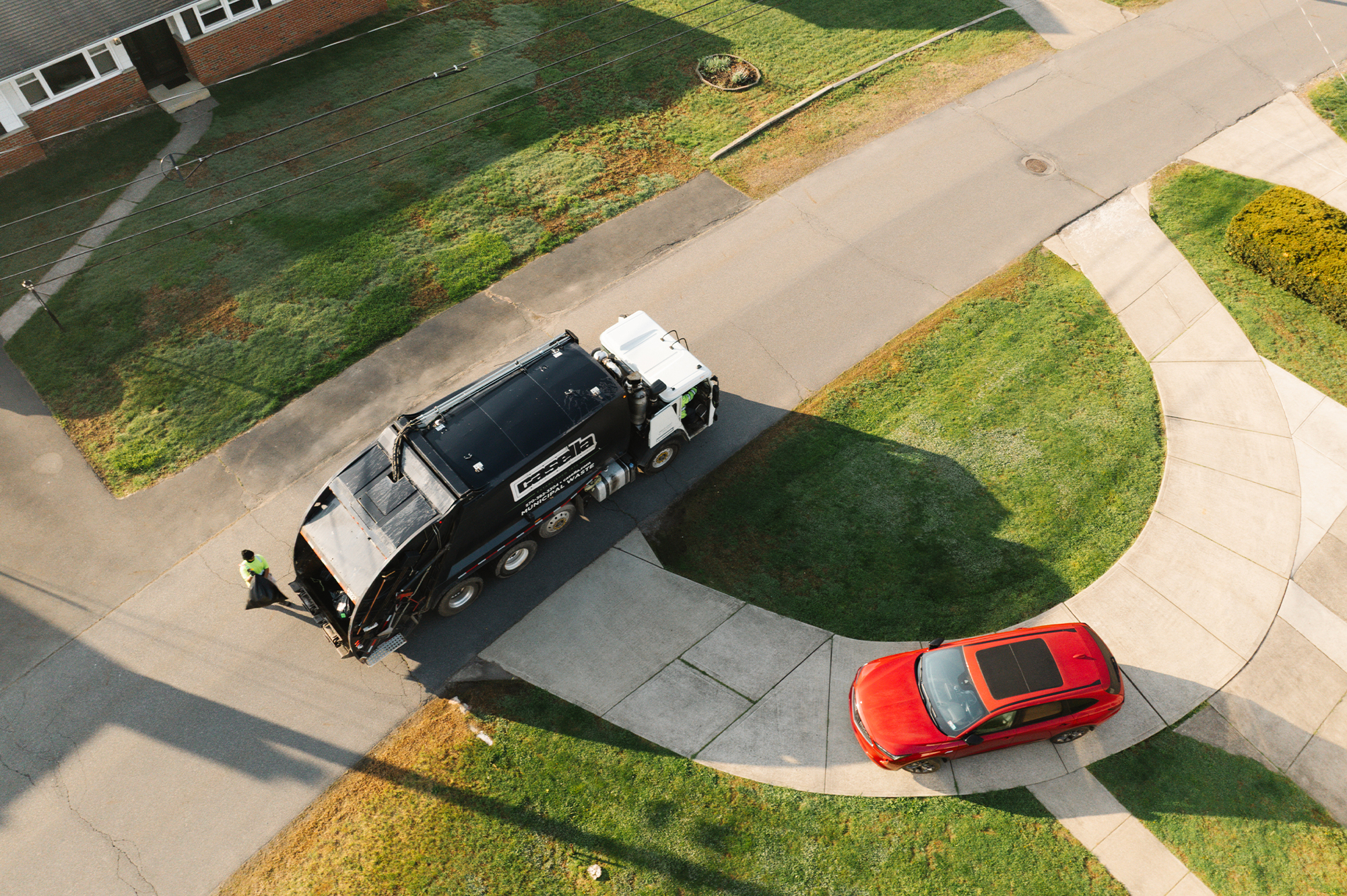 Garbage truck collecting trash on suburban street; worker nearby.