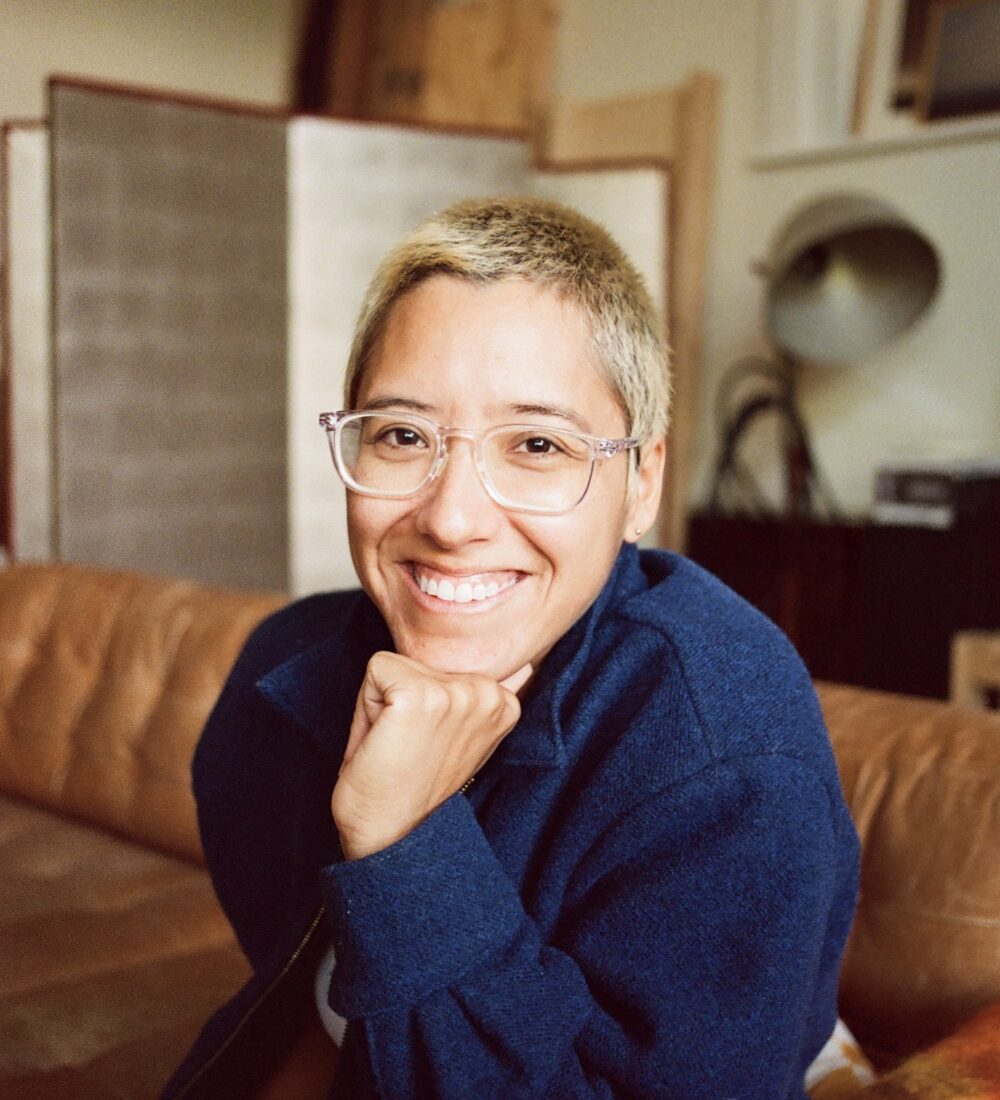 Woman with short hair and glasses smiles towards the camera.
