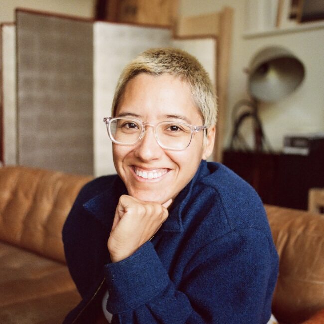 Woman with short hair and glasses smiles towards the camera.