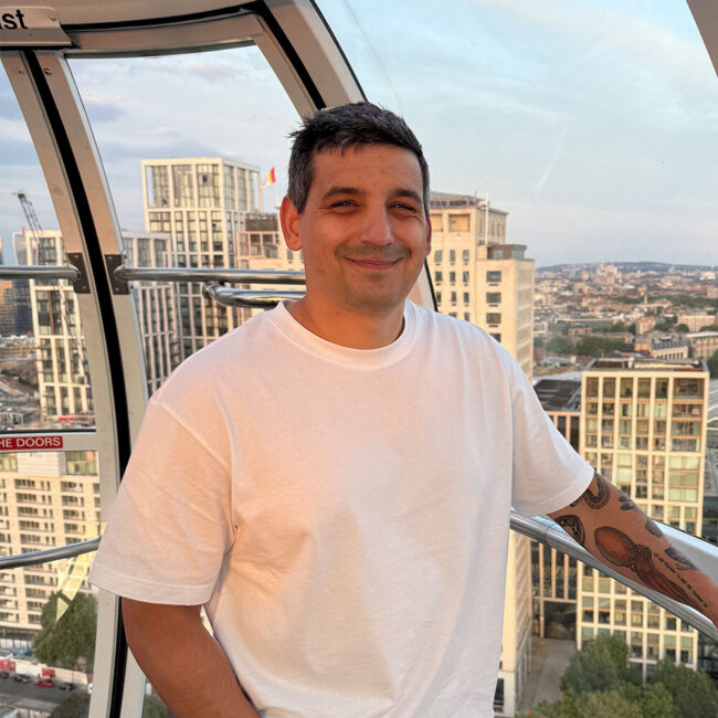 A man in a white shirt smiles at the camera with a city skyline behind him.